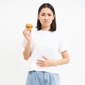 Portrait of asian woman feeling pain in stomach, discomfort after food, holding cupcake and looking unhappy, white background Portrait of asian woman feeling pain in stomach, discomfort after food, holding cupcake and looking unhappy, white background.